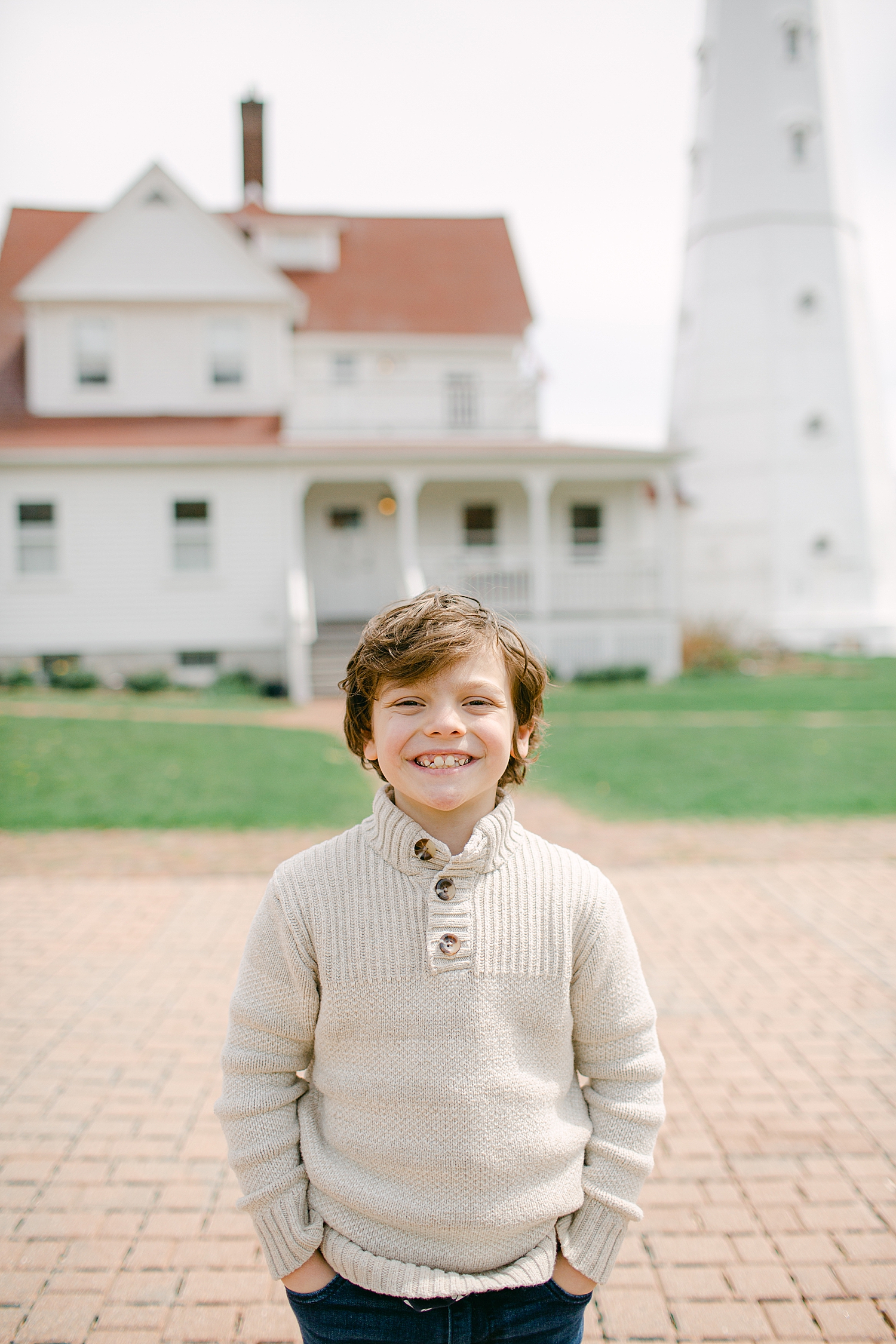 Young boy in tan sweater smiling at family photos at North Point Lighthouse in Lake Park, Milwaukee.