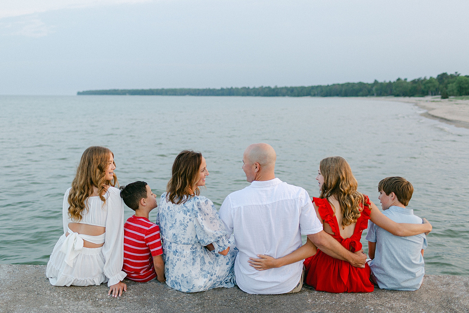 A family in coordinating outfits of red, white, and blue sitting on the pier at their Sturgeon Bay Canal Light Family Session