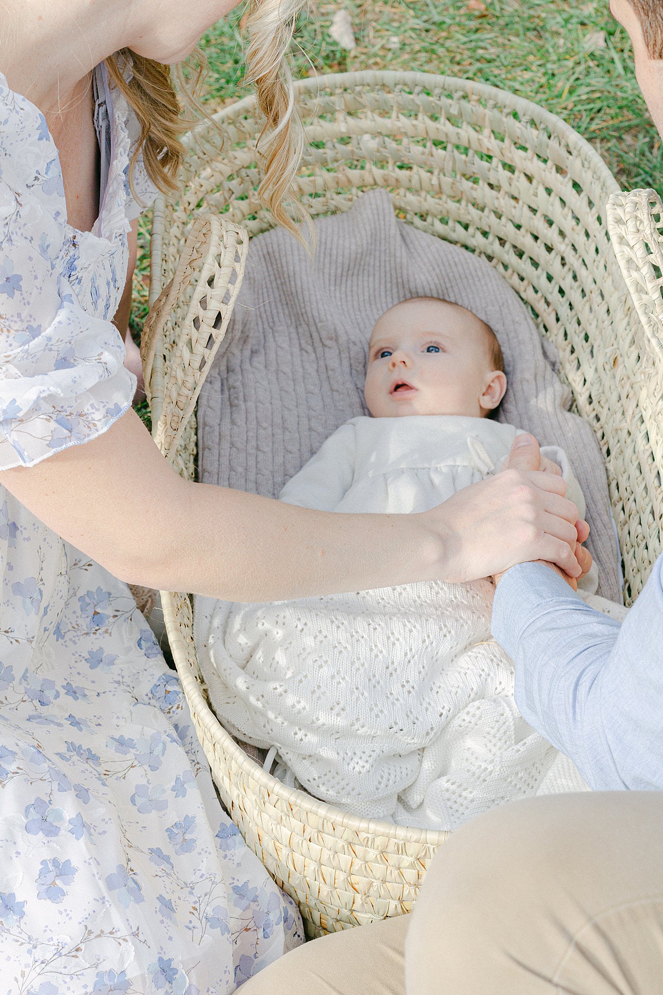 Mom, Dad, and baby holding hands while baby is in a moses basket at a Newborn Session in Green Bay